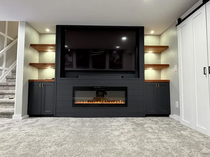 Custom navy built-in with electric fireplace, cabinets and lit floating shelves